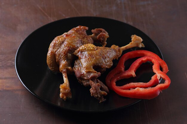 Dos muslos de pato al horno en un plato negro con pimiento rojo sobre un fondo oscuro Deliciosos muslos de pato con un primer plano de corteza dorada