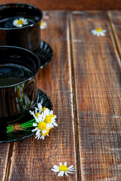 Dos negro taza de té con manzanilla en el fondo de la tabla de madera.