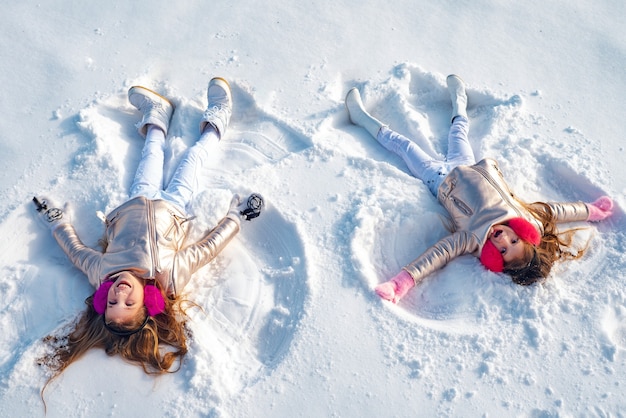 Dos niña haciendo ángel de nieve mientras está acostado sobre la nieve. Niña feliz en un ángel de nieve muestra