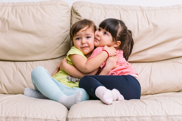 Dos niñas abrazándose, sentada en un sofá de color crema
