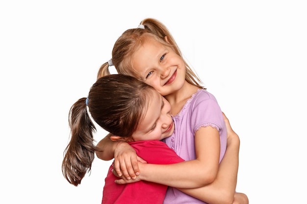 Foto dos niñas abrazándose y sonriendo sobre fondo blanco.