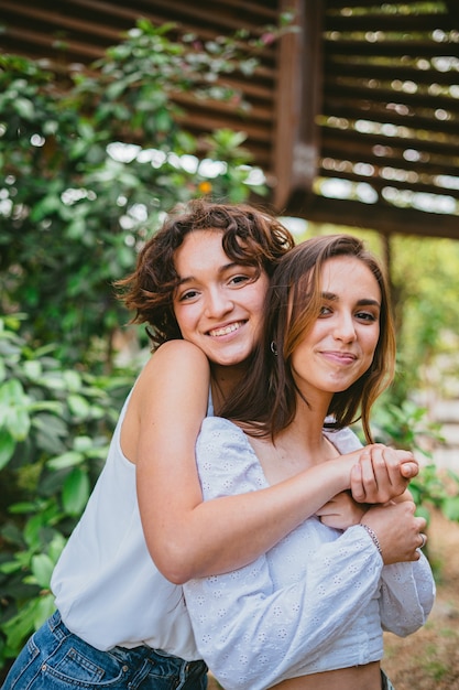 Dos niñas adolescentes abrazándose y sonriendo rodeadas de plantas.