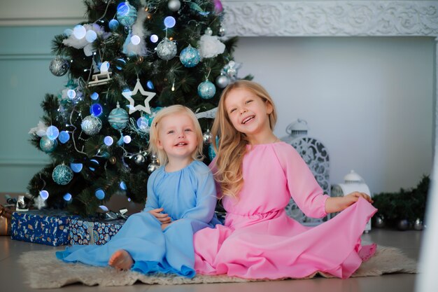 dos niñas al lado del árbol de navidad