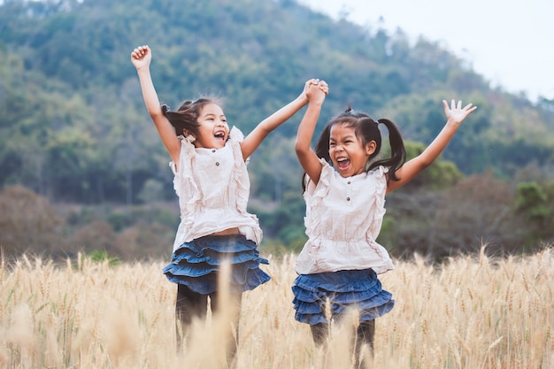 Dos niñas asiáticas felices que se divierten para jugar y saltar juntas en el campo de cebada