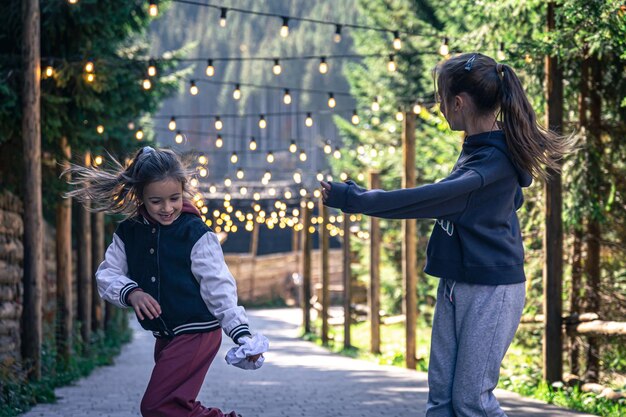 Dos niñas bailan en el bosque sobre un fondo borroso con bombillas