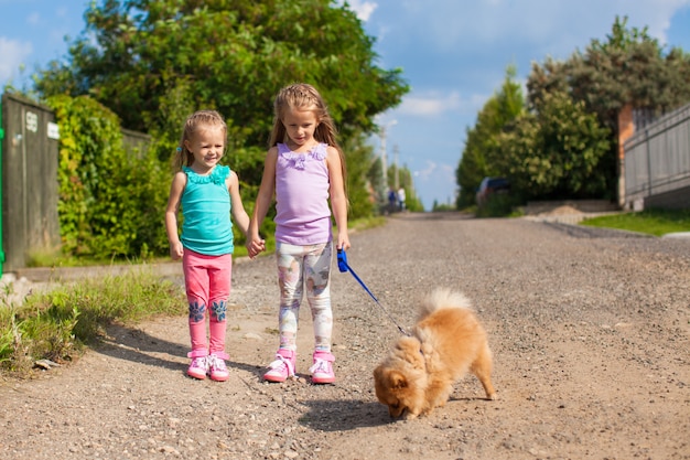 Dos niñas caminando con un perro pequeño con una correa al aire libre