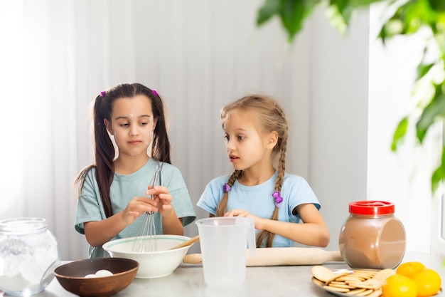 Dos niñas en la cocina preparan la comida, un postre para la familia. A medida que aprenden a cocinar, empiezan a jugar con la harina y a sonreír entre ellos. Concepto de: clases de cocina, familia, educación.