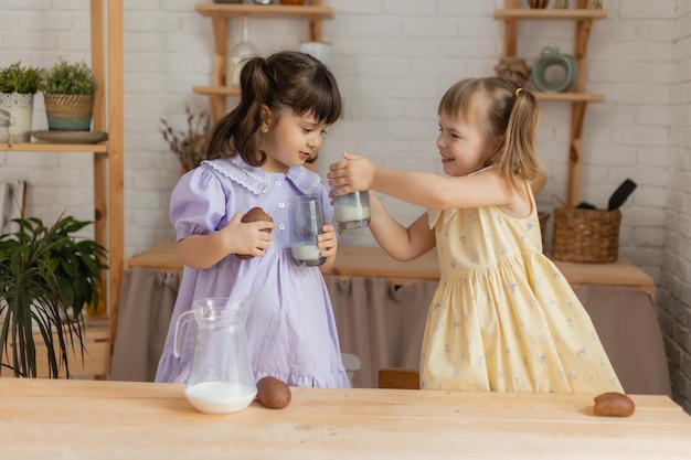 dos niñas en la cocina vierten leche de una jarra de vidrio en vasos y beben