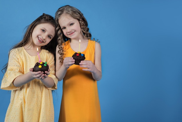 Dos niñas con cupcakes y velas festivas sobre un fondo brillante