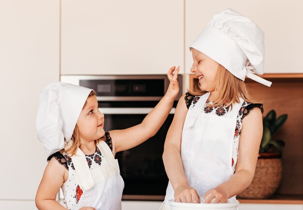 Dos niñas divertidas con gorros de chef blancos juegan con harina en una cocina ligera