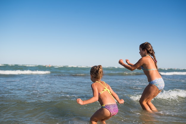 Dos niñas divertidas saltan en las ruidosas olas del mar y disfrutan de las tan esperadas vacaciones en un cálido día soleado de verano