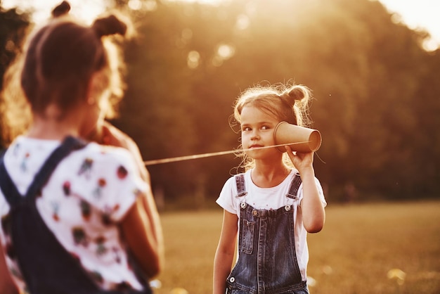 Dos niñas están de pie en el campo y hablando usando un teléfono de cuerda