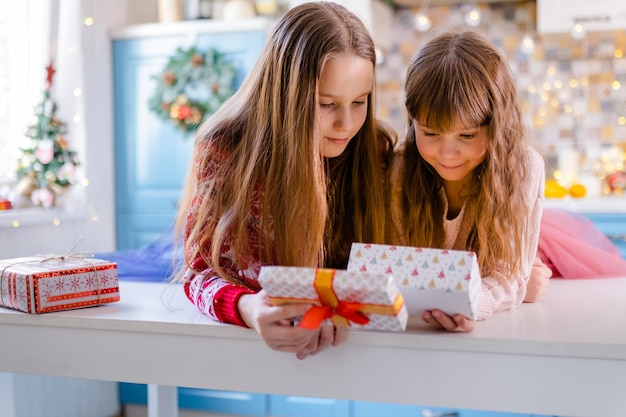 Dos niñas están sentadas en la cocina y agitando cajas con regalos.