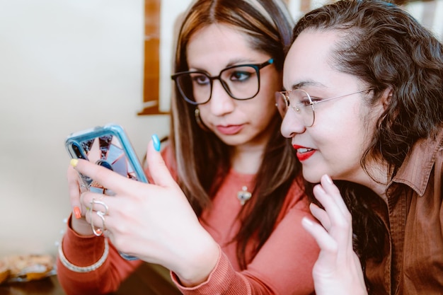 Dos niñas están sentadas y mirando un teléfono celular, están mirando de cerca sus teléfonos celulares