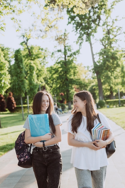 Dos niñas estudiantes sonrientes felices están caminando y hablando entre sí en el campus en un día cálido y soleado. Enfoque selectivo suave.