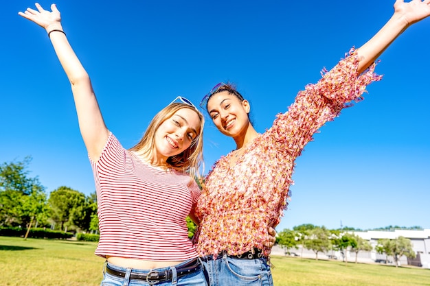 Dos niñas felices abrazándose con los brazos abiertos sonriendo mirando en un campo del parque de la ciudad