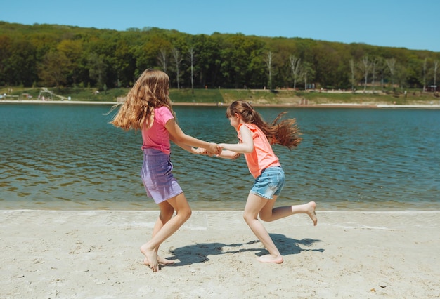 Dos niñas felices se divierten y corren alegremente en la playa saltan sobre la arena