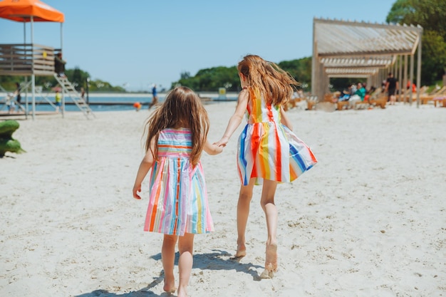 Dos niñas felices se divierten y corren alegremente en la playa saltan sobre la arena