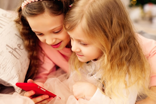 Dos niñas felices están encantadas de ver fotos en su teléfono móvil