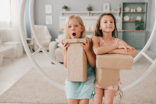 Dos niñas felices en hermosos vestidos sentados en el columpio con cajas de regalo en sus manos en la habitación de los niños