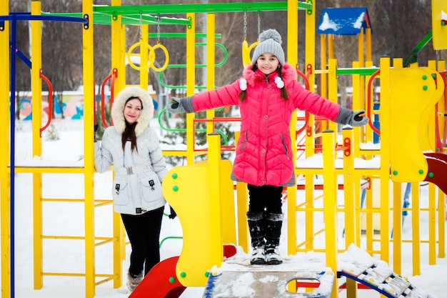 Dos niñas felices, madre e hija jugando en un patio de recreo en el día helado de invierno.