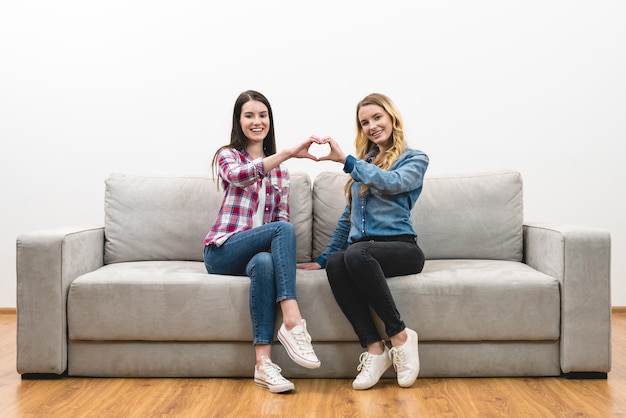 Las dos niñas felices muestran el símbolo del corazón en el fondo de la pared blanca