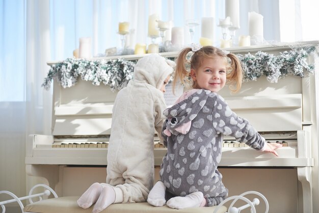 Dos niñas felices en pijama tocan el piano el día de Navidad