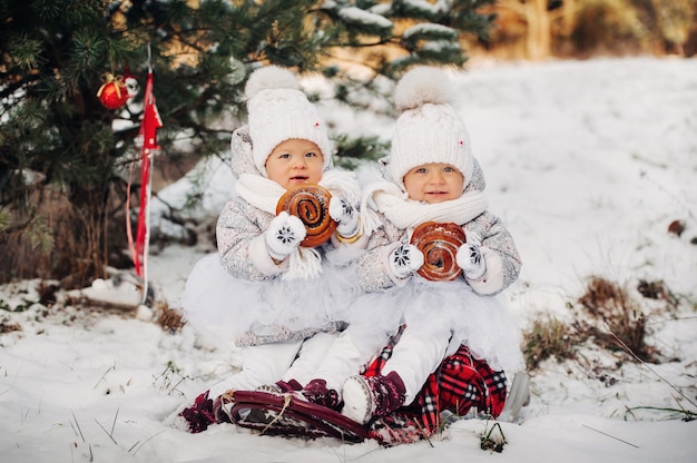 Dos niñas gemelas en trajes blancos se sientan y comen grandes bollos en el invierno afuera