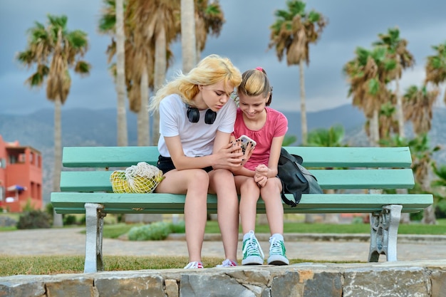 Dos niñas hermanas adolescentes y preadolescentes miran un teléfono inteligente