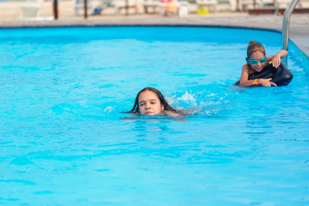 Dos niñas de las hermanas pequeñas están nadando en una gran piscina con agua azul clara mía cerca del hotel