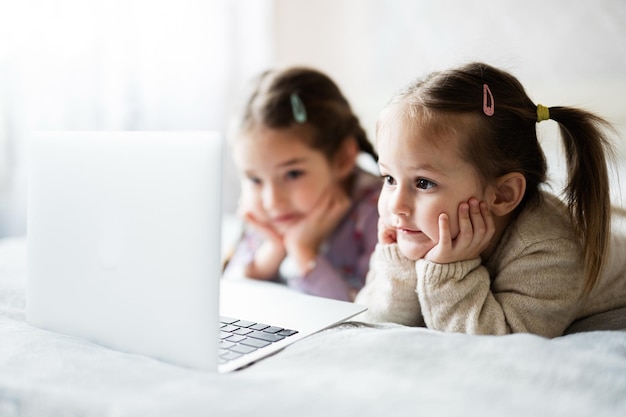 Dos niñas hermanas viendo en la computadora portátil Tecnología y concepto de hogar