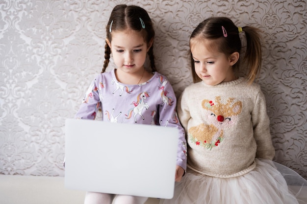 Dos niñas hermanas viendo en la computadora portátil Tecnología y concepto de hogar