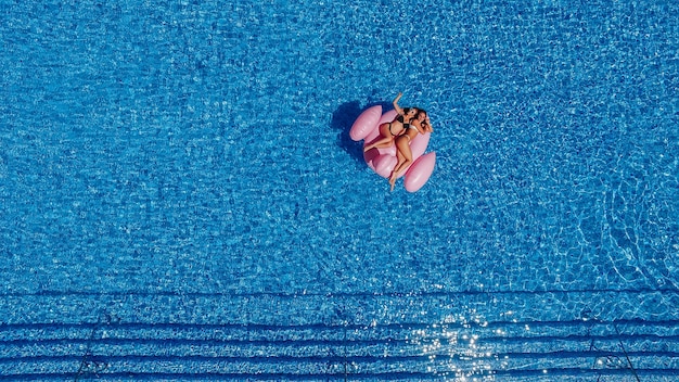 Dos niñas hermosas jóvenes felices con hermosas figuras nadan en la piscina de flamencos