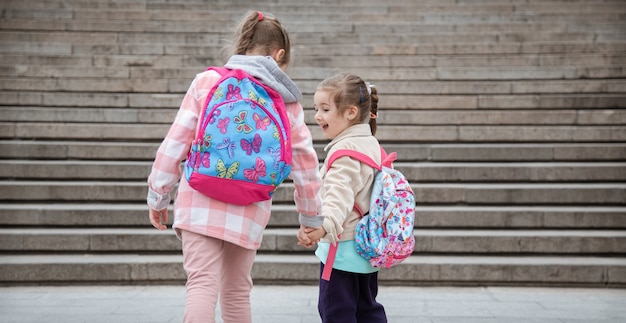 Dos niñas con hermosas mochilas en la espalda van juntas a la escuela. Concepto de amistad infantil.