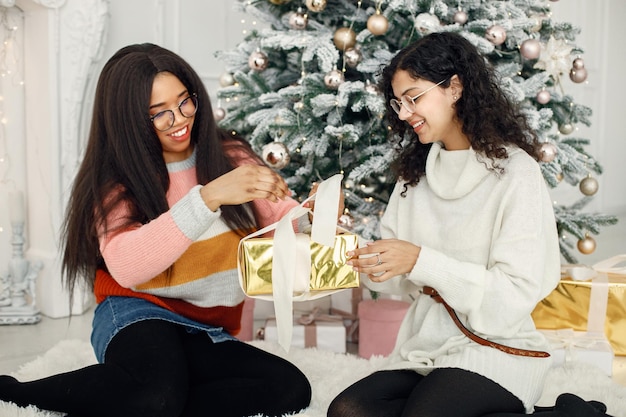 Dos niñas indias con anteojos sentadas cerca del árbol de Navidad