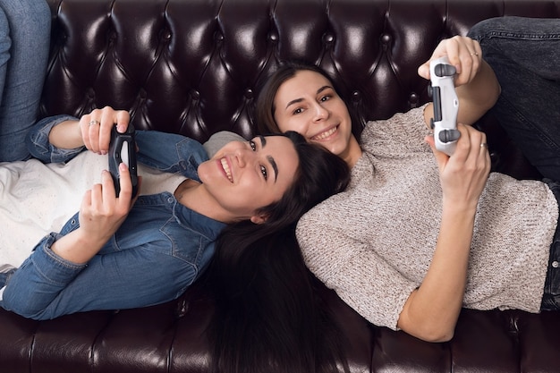 Dos niñas juegan a la consola de juegos, las mujeres alegres descansan en casa. Foto de alta calidad