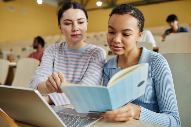 Dos niñas leyendo libros de texto y usando una computadora portátil durante el trabajo en equipo en la conferencia