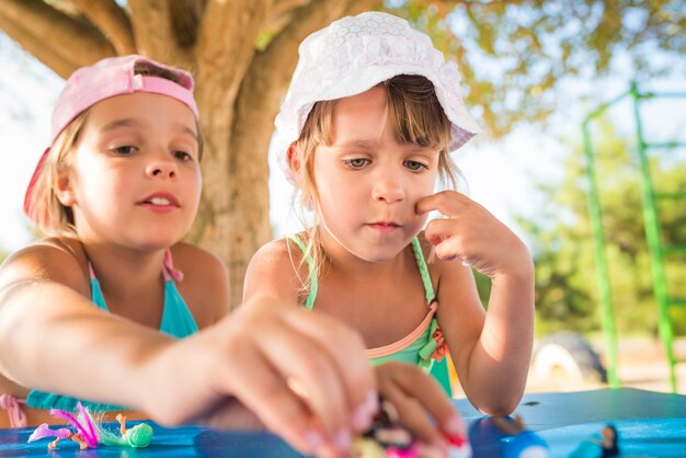 Dos niñas lindas jugando muñecas al aire libre mientras se relaja en la playa en un caluroso día de verano. El concepto de juegos activos para niños.