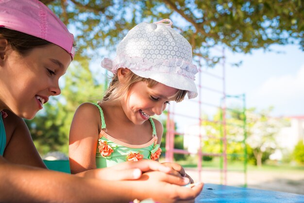 Dos niñas lindas jugando muñecas al aire libre mientras se relaja en la playa en un caluroso día de verano