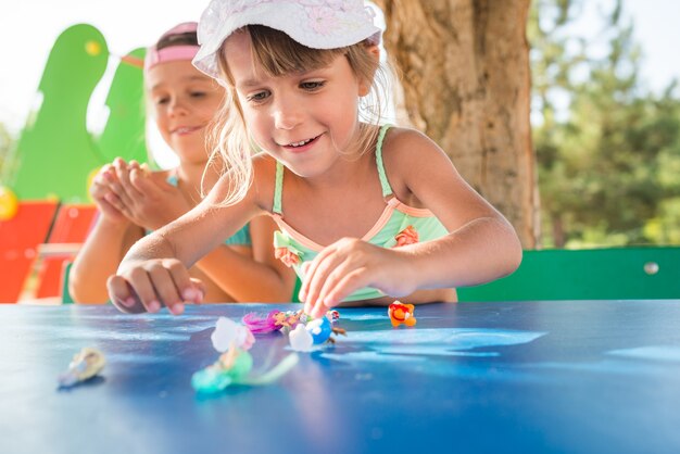 Dos niñas lindas jugando muñecas al aire libre mientras se relaja en la playa