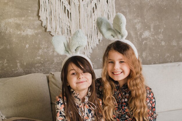Dos niñas lindas con orejas de conejo están sentadas en el sofá con canastas de Pascua