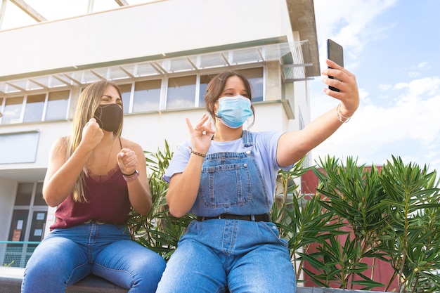 Dos niñas con máscaras hablando en lenguaje de señas en la cámara de su teléfono inteligente