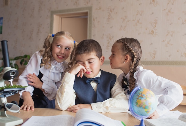 Dos niñas y un niño en la escuela en un escritorio estudiando biología y geografía discutiendo la tarea