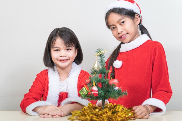 Dos niñas de niños asiáticos usan Navidad Santa Claus decorando el árbol de Navidad. Concepto De Vacaciones De Navidad Stock Photo