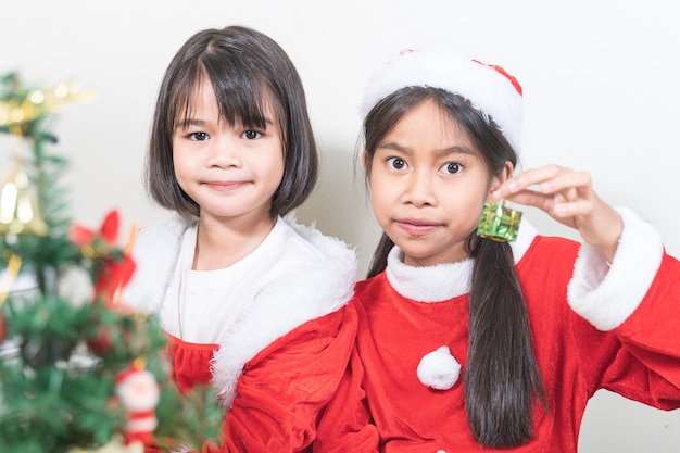 Dos niñas de niños asiáticos usan Navidad Santa Claus decorando el árbol de Navidad. Concepto De Vacaciones De Navidad Stock Photo