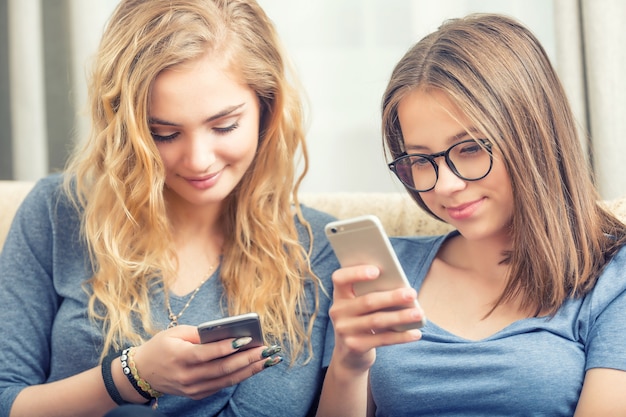 Dos niñas o hermanas adolescentes que usan teléfonos inteligentes en la sala de estar.