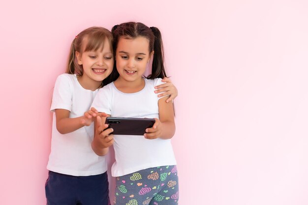 Foto dos niñas pequeñas con un teléfono inteligente en un fondo rosa