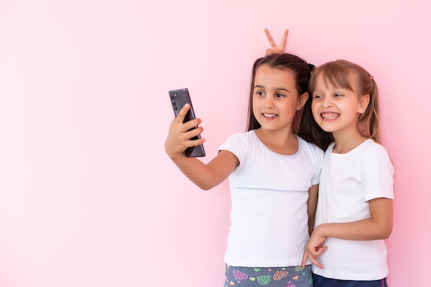 dos niñas pequeñas con un teléfono inteligente en un fondo rosa