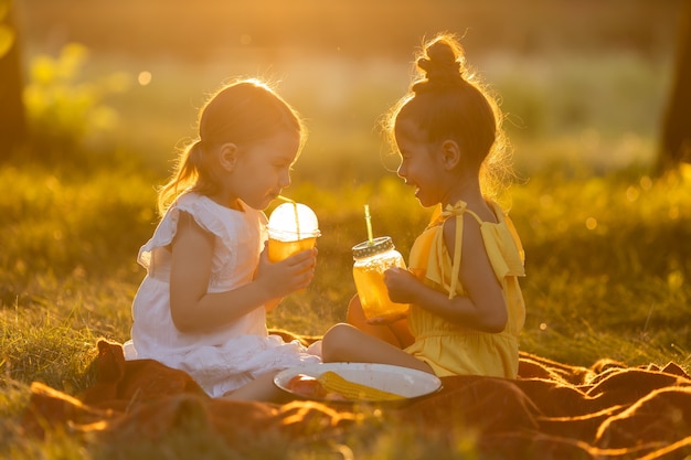 Dos niñas de raza mixta beben batidos en el jardín al aire libre comida libre de OMG Concepto de un saludable