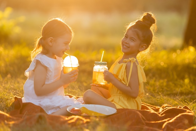 Dos niñas de raza mixta beben batidos en el jardín al aire libre comida libre de OMG Concepto de un saludable